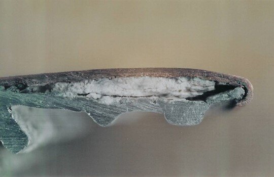 Close-up cross-section of copper cladding over aluminum showing white corrosion products on the aluminum