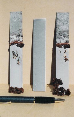 Aluminum test strips after copper sulfate exposure showing copper deposits, severe thinning, and perforation